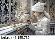 An exquisite scene done in a winter style with elements of a Russian palace setting. A woman dressed in a richly decorated snow-white outfit holds a small bird in her hands, as if protecting it. She is wearing a luxurious fur hat with patterns, a long warm coat with embroidery and fur trim. Her hair is neatly styled, and her face reflects thoughtfulness and calm. She stands on a balcony with intricate forged patterns and carved columns dotted with frost patterns. Around her, snow flowers intertwine with branches, creating a feeling of a winter fairy tale. The atmosphere of the image conveys a feeling of nobility, coldness and romantic mystery. Стоковое AI-изображение, AI-художник Анна Кривицкая / Фотобанк Лори