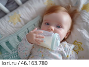A newborn enjoys feeding while lying comfortably in a cozy nursery setting during the day. Стоковое AI-изображение, AI-художник Sergey Grishin / Фотобанк Лори