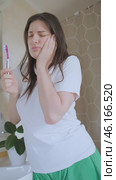 Tooth pain makes her hold her cheek, but oral care is important. Girl brushes her teeth in the bathroom despite cheek pain and discomfort. Стоковое видео, видеограф Svetlana Golovco / Фотобанк Лори