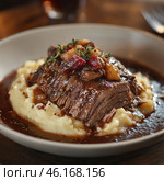 A sophisticated dish featuring a tender, simmered steak served on a bed of fluffy mashed potatoes. The meat is a rich brown with a luscious glaze of sauce that generously coats the dish. Finely chopped vegetables and bacon bits are added on top, giving the dish additional texture and flavor. A decorative sprig of fresh herbs completes the composition. The atmosphere of the photo is cozy, with warm lighting, reminiscent of a fine dining restaurant. Стоковое AI-изображение, AI-художник Анна Кривицкая / Фотобанк Лори