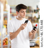 Male buyer checks suitability - scans QR code on jar of soy sauce label in grocery store. Стоковое фото, фотограф Яков Филимонов / Фотобанк Лори