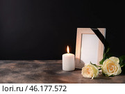 Blank funeral frame, candle and flowers on table against black background. Стоковое фото, фотограф Pixel_shot / Фотобанк Лори