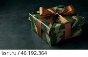 The concept of Defender of the Fatherland Day on February 23. Gift camouflage box with a festive satin ribbon bow on a dark green background. Стоковое AI-изображение, AI-художник Photojuli / Фотобанк Лори
