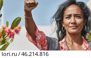 Middle aged latin american woman with raised fist of empowerment, strength and women solidarity, International Womens Day concept. Стоковое AI-изображение, AI-художник Анастасия Золотницкая / Фотобанк Лори