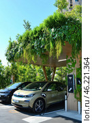 Electric cars charging at station with green roof in urban setting. Стоковое AI-изображение, AI-художник Юрий Поздников / Фотобанк Лори
