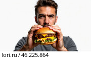 A Man Enjoying a Delicious Cheeseburger in a Studio Setting, Highlighting the Juicy Ingredients and Enticing Flavors. Стоковое AI-изображение, AI-художник Sergey Grishin / Фотобанк Лори