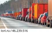 Long line of trucks and cars along highway in rural area during winter. Стоковое AI-изображение, AI-художник Olga Didraga / Фотобанк Лори
