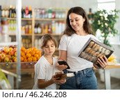 Girl with mother customers at shop scans QR code on sweets package using phone camera. Стоковое фото, фотограф Яков Филимонов / Фотобанк Лори