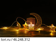 Arabic candle holder with glowing candle and garland on table against dark background. Стоковое фото, фотограф Pixel_shot / Фотобанк Лори