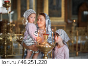 Young mother and her little blond Caucasian daughter with candles in Orthodox Russian Church. Стоковое фото, фотограф Арзюков Вадим Николаевич / Фотобанк Лори