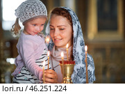 Russian beautiful woman in a scarf and with red hair holding a little girl and lights a candle in front of an icon in the Russian Orthodox Church. Стоковое фото, фотограф Арзюков Вадим Николаевич / Фотобанк Лори