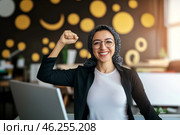 Muslim middle eastern woman in office with raised fist of empowerment, strength and women solidarity, International Womens Day concept. Стоковое AI-изображение, AI-художник Анастасия Золотницкая / Фотобанк Лори