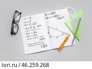 Copybook with maths formulas, glasses and stationery on grey background. Стоковое фото, фотограф Pixel_shot / Фотобанк Лори
