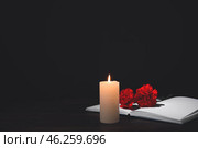 Book with carnation flowers and candle on table against dark background. Стоковое фото, фотограф Pixel_shot / Фотобанк Лори