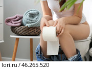 Young woman with soft paper sitting on toilet bowl in restroom. Стоковое фото, фотограф Pixel_shot / Фотобанк Лори