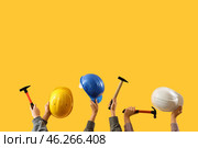 Female hands holding safety hardhats and hammers on yellow background. Стоковое фото, фотограф Pixel_shot / Фотобанк Лори