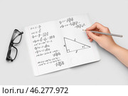 Woman writing maths formulas in copybook with pencil on grey background. Стоковое фото, фотограф Pixel_shot / Фотобанк Лори