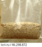 A bag of buckwheat groats for cooking. The groats are packaged in a transparent plastic bag with small holes designed for easy cooking in boiling water. Buckwheat grains have light brown and cream shades, a characteristic uneven texture. The background is slightly blurred, creating an emphasis on the product. Стоковое фото, фотограф Анна Кривицкая / Фотобанк Лори