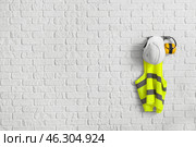 Reflective vest and hearing protectors on white brick wall. Стоковое фото, фотограф Pixel_shot / Фотобанк Лори