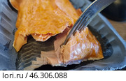 A piece of smoked fish, probably salmon or trout, in plastic packaging. The fish has a rich golden-orange hue, typical of smoking. You can see layers of tender and juicy fillet, which are easily separated by a fork. The shiny surface indicates the oily structure of the product. This delicacy is often served as an appetizer, used in sandwiches or salads. Стоковое фото, фотограф Анна Кривицкая / Фотобанк Лори