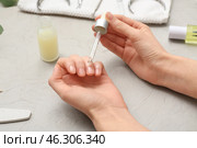 Female hands applying cuticle oil onto fingernails on grey grunge background, closeup. Стоковое фото, фотограф Pixel_shot / Фотобанк Лори