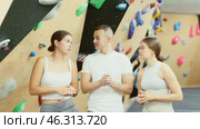 Group of positive friendly novice climbers, young women and man, standing in training room against backdrop of bouldering wall, discussing with interest routes and techniques of climbing. Стоковое видео, видеограф Яков Филимонов / Фотобанк Лори