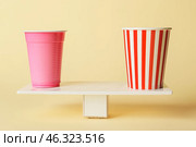 Plastic and paper cups on teeterboard against color background. Concept of balance. Стоковое фото, фотограф Pixel_shot / Фотобанк Лори