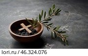 Religion, faith, liturgy, Ash Wednesday. Great lent. A wooden cross, a ceremonial bowl made of ash and an olive branch on a gray background. Стоковое AI-изображение, AI-художник Photojuli / Фотобанк Лори