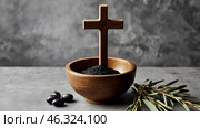 Religion, faith, liturgy, Ash Wednesday. Great lent. A wooden cross, a ceremonial bowl made of ash and an olive branch on a gray background. Стоковое AI-изображение, AI-художник Photojuli / Фотобанк Лори