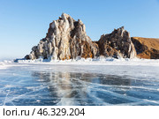 Winter landscape of frozen Baikal Lake with famous Shamanka rock - natural landmark Olkhon Island from blue clear ice with cracks on sunny day in February. Cape Burkhan - place of attraction for tourists. Стоковое фото, фотограф Виктория Катьянова / Фотобанк Лори