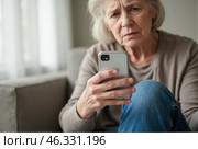 Senior woman holding smartphone while feeling anxious and sad, upset about losing savings due to scam, seated in living room, reflecting on financial loss, distressed expression visible. Стоковое AI-изображение, AI-художник Павел Муравьев / Фотобанк Лори