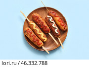 Wooden plate of tasty corn dogs with different sauces on blue background. Стоковое фото, фотограф Pixel_shot / Фотобанк Лори