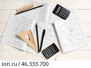 Copybooks with handwritten maths formulas, calculators and stationery on white wooden background. Стоковое фото, фотограф Pixel_shot / Фотобанк Лори