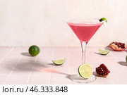 Glass of Cosmopolitan cocktail with lime and pomegranate on pink tile table. Стоковое фото, фотограф Pixel_shot / Фотобанк Лори