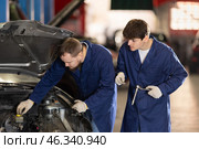 Two auto mechanics work together to diagnose an engine under the hood of a car in repair shop. Стоковое фото, фотограф Яков Филимонов / Фотобанк Лори
