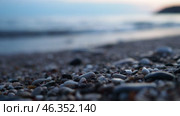 Waves gently lap at rocky shore during stunning sunset over ocean. Blue sunlight reflects off waves as they roll onto shore, creating tranquil atmosphere at sunset by sea. Focus on pebbles and stones. Стоковое видео, видеограф Юлия Петровская / Фотобанк Лори
