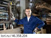 Male employee of workshop stands next to iron rails of workpieces, measures length. Стоковое фото, фотограф Яков Филимонов / Фотобанк Лори