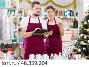Bearded man and woman sellers restock of goods using tablet in store decorated for New Year holiday. Стоковое фото, фотограф Яков Филимонов / Фотобанк Лори