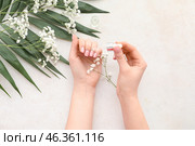 Female hands with bottle of cuticle oil, gypsophila flowers and palm leaf on light background. Стоковое фото, фотограф Pixel_shot / Фотобанк Лори