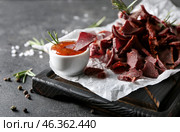 Board with spicy beef jerky and sauce on dark background. Стоковое фото, фотограф Pixel_shot / Фотобанк Лори