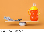 Dollar banknotes and baby bottle on teeterboard against color background. Concept of balance. Стоковое фото, фотограф Pixel_shot / Фотобанк Лори