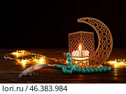 Arabic candle holder with glowing candle, garland and tasbih on table against dark background. Стоковое фото, фотограф Pixel_shot / Фотобанк Лори