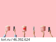 Hands with buckets of popcorn and TV remotes on pink background. Стоковое фото, фотограф Pixel_shot / Фотобанк Лори