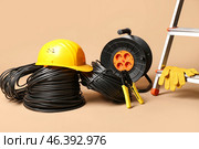 Rolled wires, crimper, hardhat and extension cable reel on beige background. Стоковое фото, фотограф Pixel_shot / Фотобанк Лори