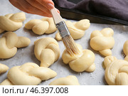 Woman greasing uncooked garlic buns with oil on baking sheet. Стоковое фото, фотограф Pixel_shot / Фотобанк Лори