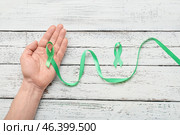 Male hand with green ribbons on light wooden background. Mitochondrial diseases and kidney cancer concept. Стоковое фото, фотограф Pixel_shot / Фотобанк Лори