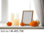 Blank frame with pumpkins and candles on mantelpiece in room, closeup. Стоковое фото, фотограф Pixel_shot / Фотобанк Лори