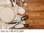 Embroidery hoop with canvas, mouline threads and scissors on brown wooden background. Стоковое фото, фотограф Pixel_shot / Фотобанк Лори