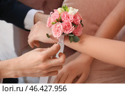 Teenage boy tying corsage around his girlfriend's wrist for prom in room, closeup. Стоковое фото, фотограф Pixel_shot / Фотобанк Лори