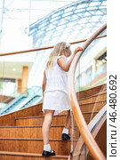 A young girl in a white dress climbs a polished wooden staircase, showcasing her playful spirit. Стоковое фото, фотограф Aleksandr Golubev / Фотобанк Лори